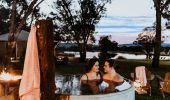 Couple relaxing in hot tub with sun setting behind them at Evamor Valley, Mudgee